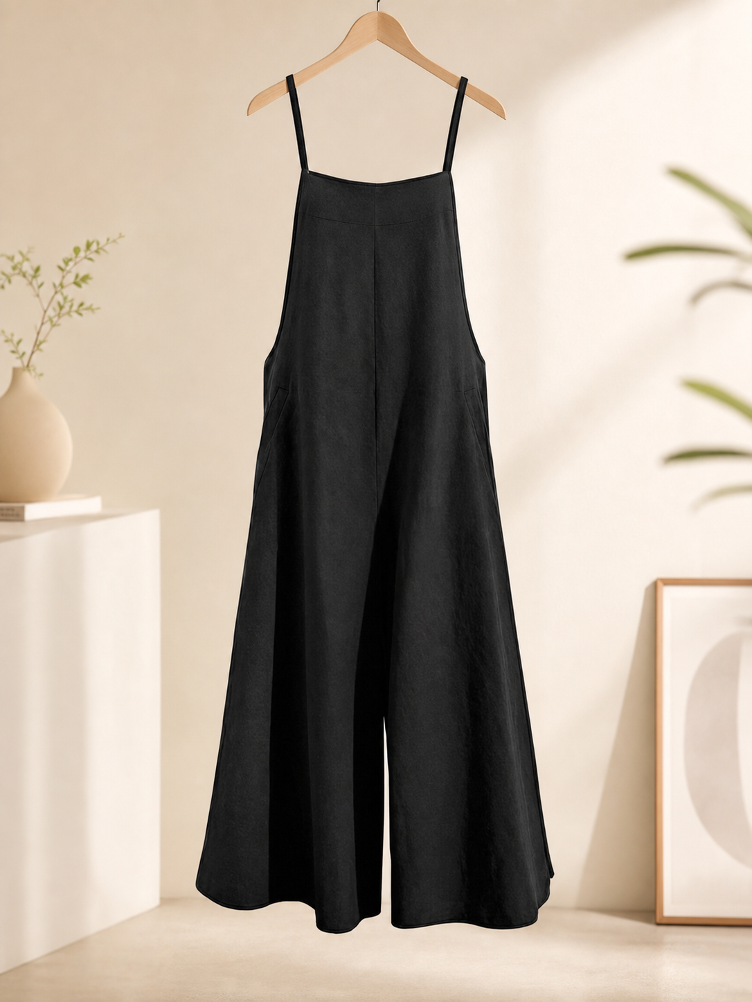 Loose black bib overalls with thin shoulder straps. The design features a simple solid black color and a straight, wide-leg silhouette with long pant legs. The upper portion is styled as a bib, while the thin shoulder straps complement the 