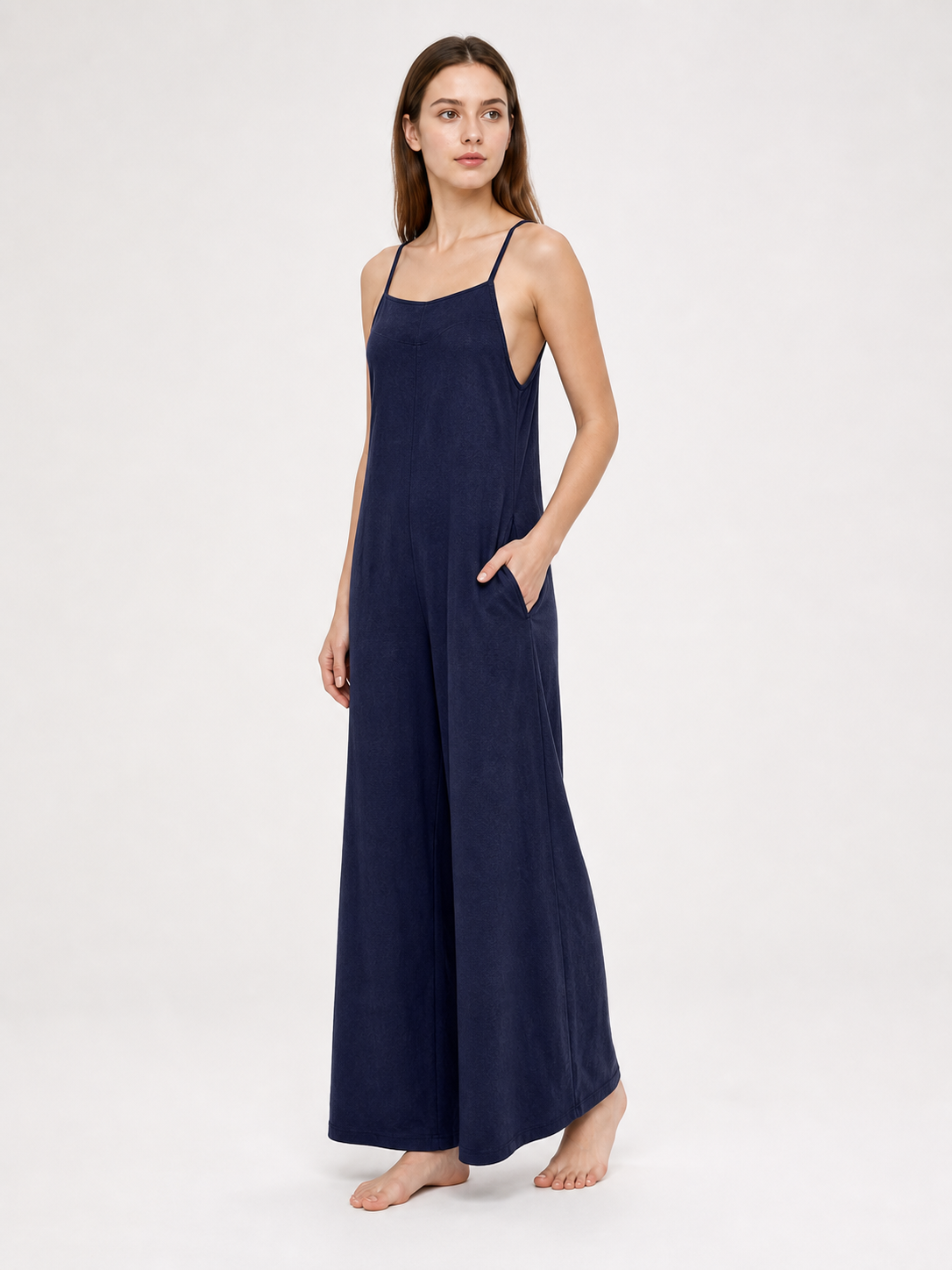 Side view of a dark blue wide-leg jumpsuit with thin straps and a side pocket, modeled barefoot against a light background