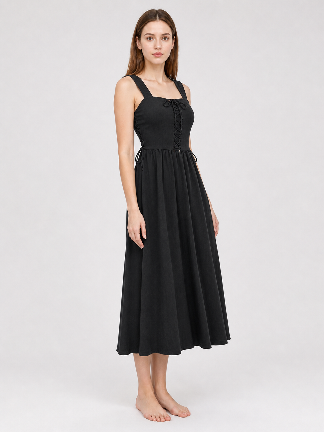 Three-quarter front view of a black midi dress, showing the fitted lace-up bodice, wide straps, side ties, and gathered skirt