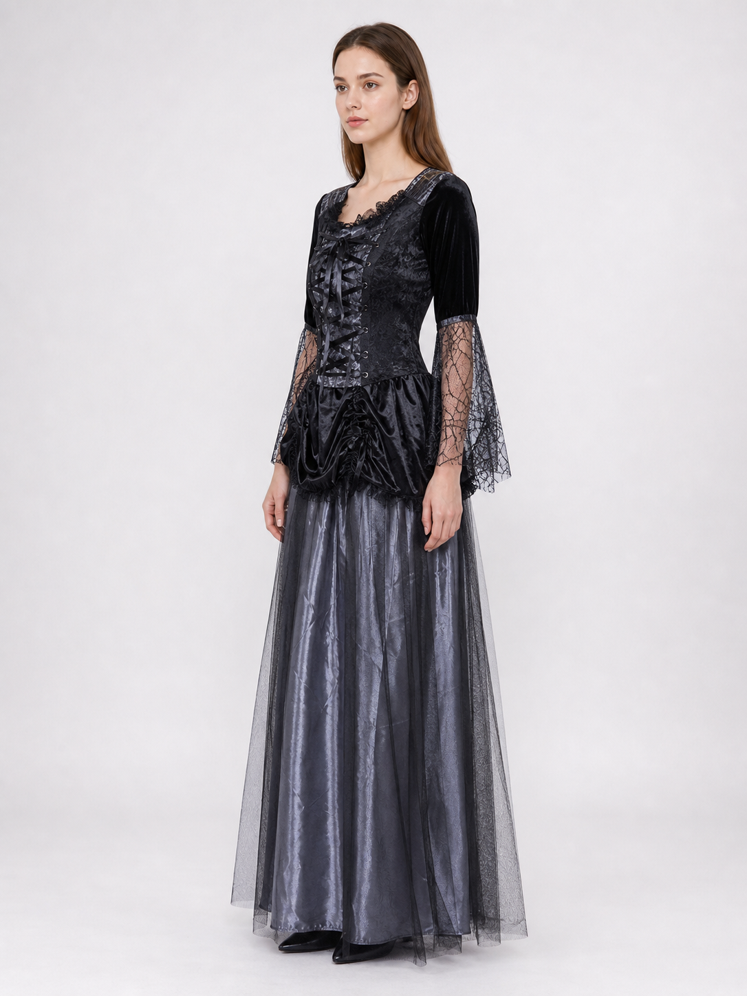 Gothic-style witch costume dress with hat for themed events. The design is mainly black and dark gray, with patterned textured fabric and sheer black accents. The look is centered on a long dress with a fitted lace-up corset, a ruffled neck