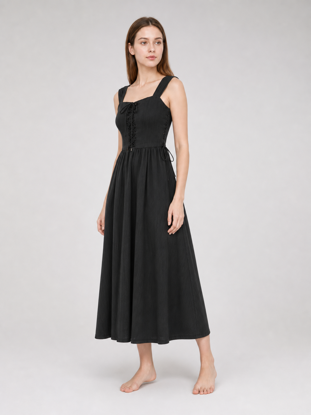 Three-quarter view of a black midi dress on a model, showing the lace-up front, wide shoulder straps, side ties, and flared midi skirt