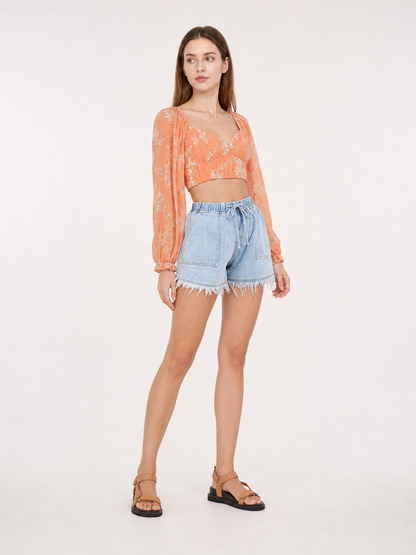 Light blue denim shorts with a drawstring waist, patch pockets and frayed hems shown in a styled indoor scene