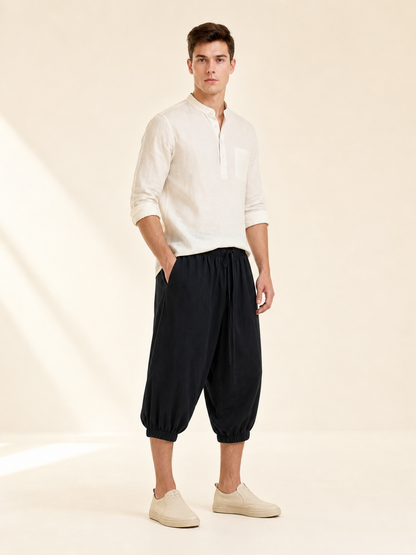 Side view of black cropped pants with a relaxed fit, elastic waist, and gathered cuffs on a model
