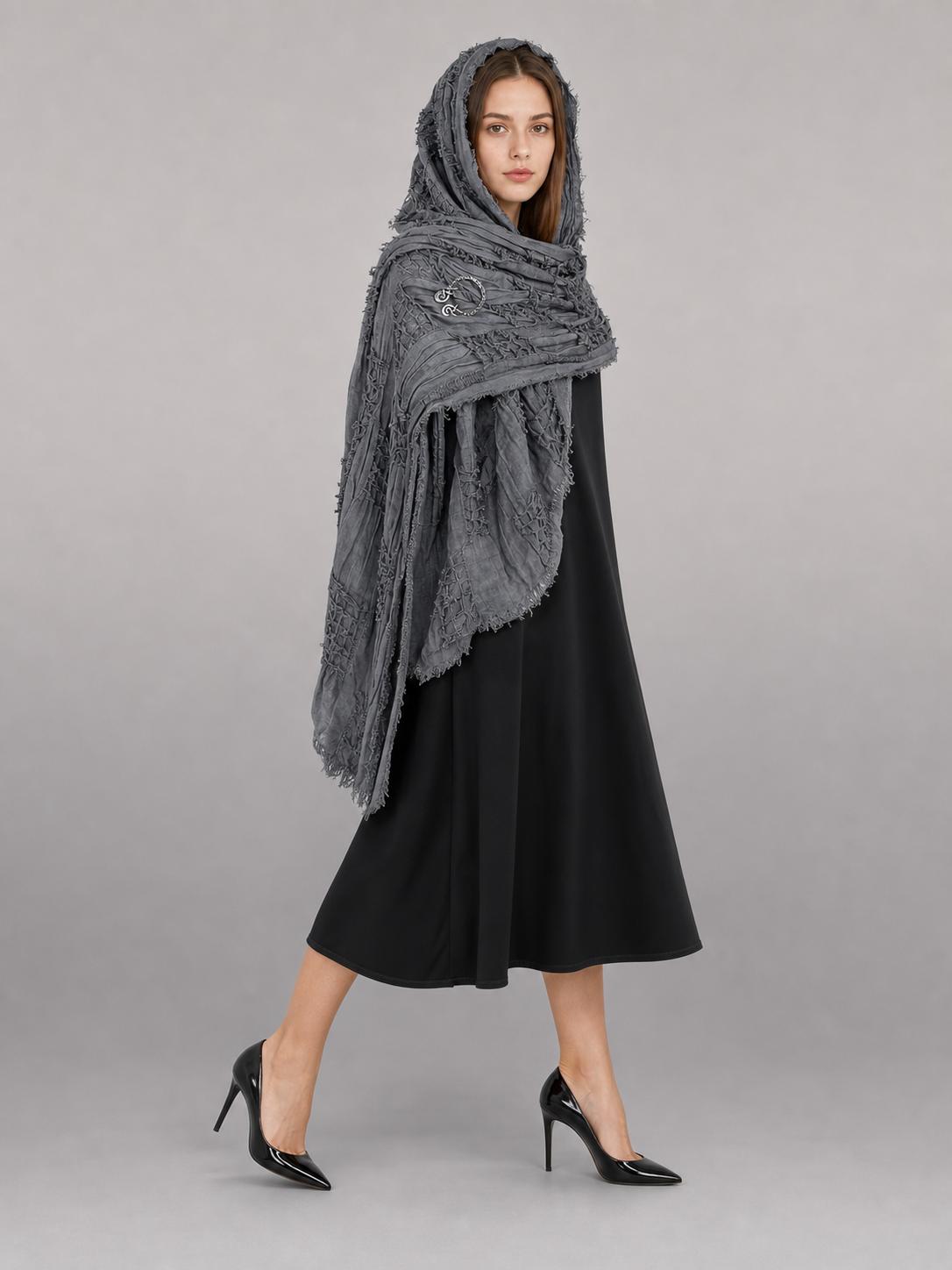 This large scarf-wrap is designed as a rectangular drape with a striking textured surface. The black-and-gray color palette is accented with lighter gray tones, giving the piece a distinctive look that pairs easily with different outfits. T