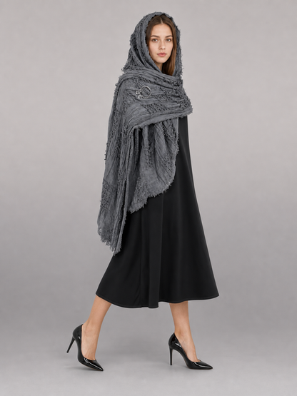 This large scarf-wrap is designed as a rectangular drape with a striking textured surface. The black-and-gray color palette is accented with lighter gray tones, giving the piece a distinctive look that pairs easily with different outfits. T