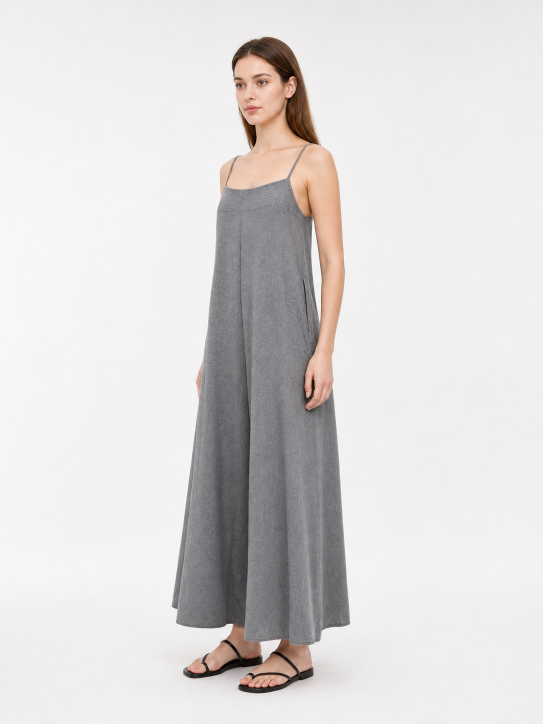 Side view of a gray wide-leg jumpsuit with thin straps and a flowing silhouette, shown full-length on a model wearing flat sandals