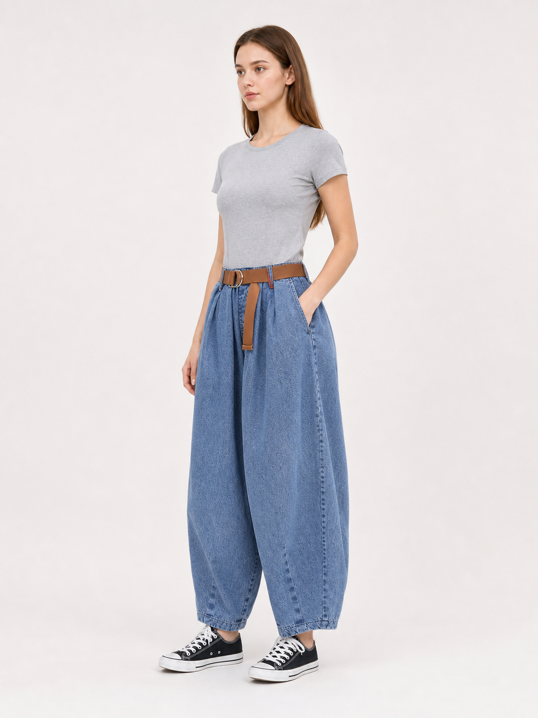 Three-quarter view of a model wearing blue denim pants with wide legs, side pockets, a brown belt, and black sneakers
