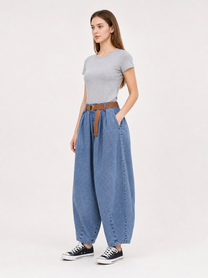 Three-quarter view of a model wearing blue denim pants with wide legs, side pockets, a brown belt, and black sneakers