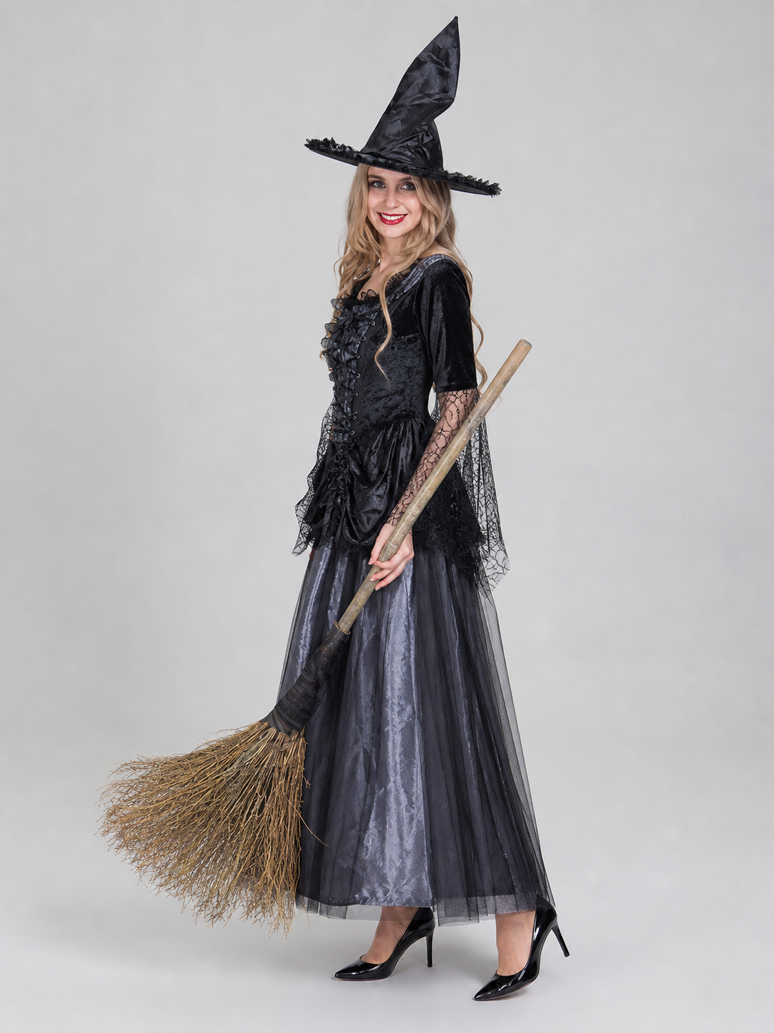 Gothic-style witch costume dress with hat for themed events. The design is mainly black and dark gray, with patterned textured fabric and sheer black accents. The look is centered on a long dress with a fitted lace-up corset, a ruffled neck