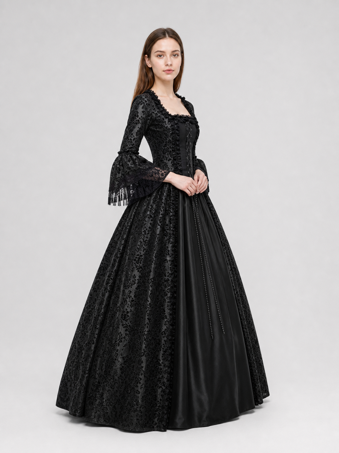 The black dress is designed in the aesthetic of a Victorian-era Gothic costume. The model features a floor-length silhouette, a fitted bodice with a square neckline, and decorative lacing or trim on the front. The long flared sleeves end in