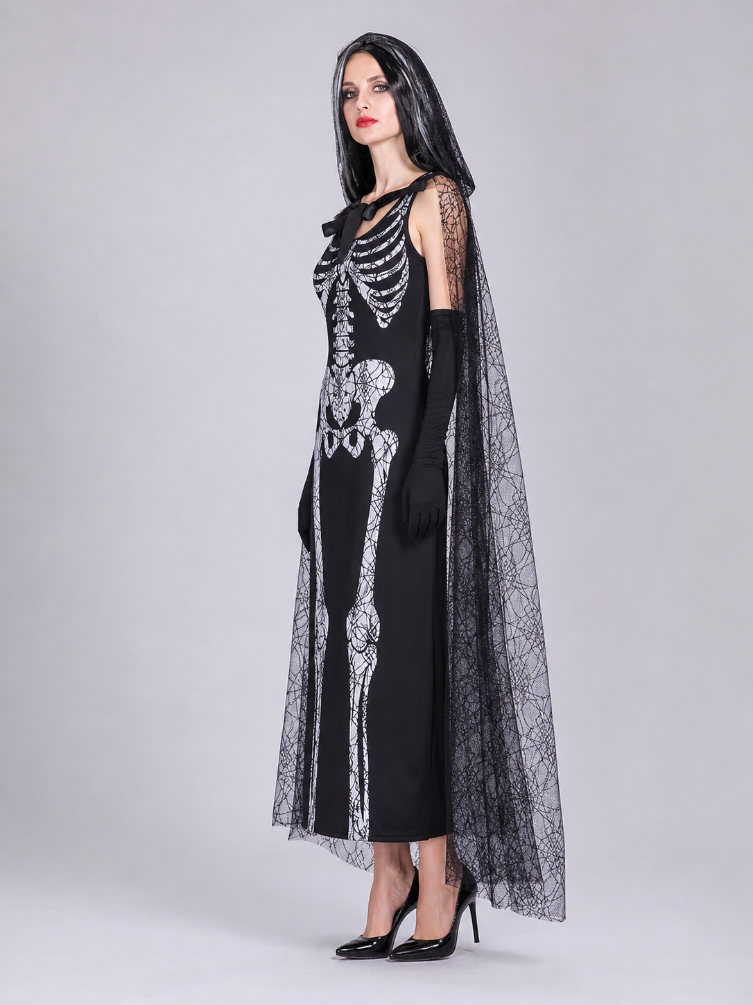 Gothic Halloween costume dress with accessories: a sleeveless black dress with a white rib and pelvic bone print, a sheer cape or veil with a spiderweb design, black gloves, and a necktie or bow detail. The look is done in black and white w