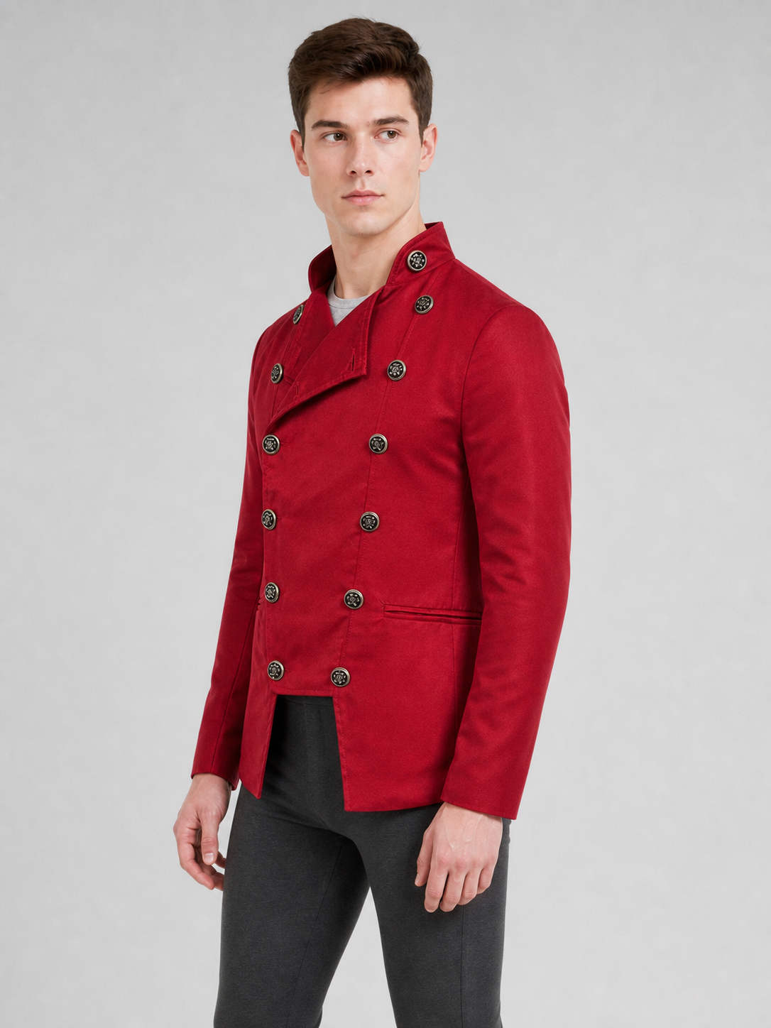 The jacket is presented in a vintage red color and designed in a military style with elements of Gothic aesthetics. The model features a distinctive front construction with a diagonal wrap, giving the garment a bold character. A double row 