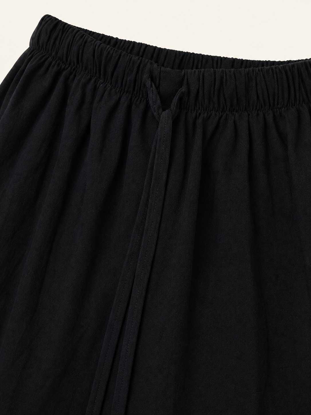 Close-up of the black pants waistband and drawstring, showing the gathered fabric and smooth woven texture