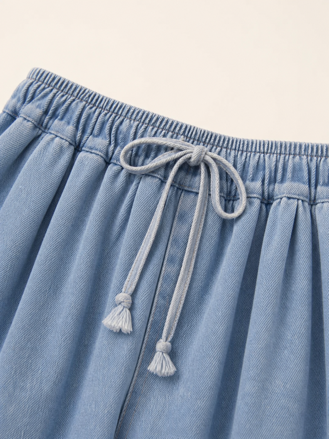 The model features a relaxed style with very wide, full-length legs that create a laid-back silhouette and suit everyday looks. The light blue shade with a subtle denim-like effect makes the piece versatile for warm weather and easy to pair