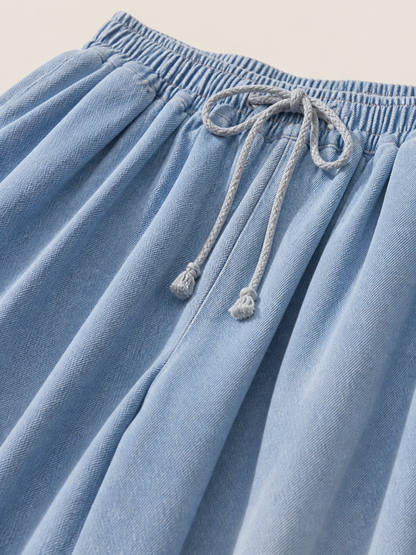 The model features a relaxed style with very wide, full-length legs that create a laid-back silhouette and suit everyday looks. The light blue shade with a subtle denim-like effect makes the piece versatile for warm weather and easy to pair