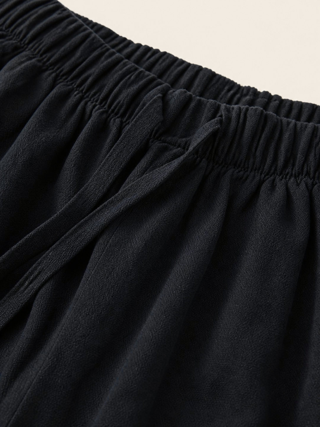 Close-up of black pants fabric near the waist and side pocket opening, showing gathered details and a soft texture