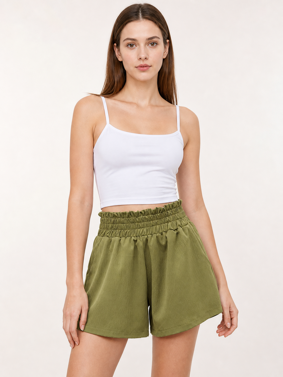 Front view of olive green shorts on a model, showing the high gathered waistband, side pockets, relaxed fit, and lightweight fabric look