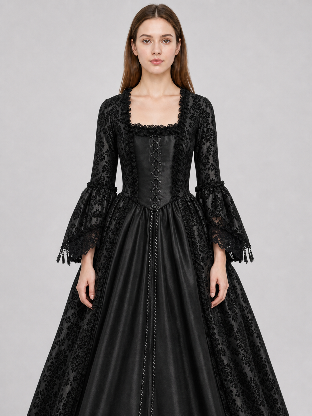 The black dress is designed in the aesthetic of a Victorian-era Gothic costume. The model features a floor-length silhouette, a fitted bodice with a square neckline, and decorative lacing or trim on the front. The long flared sleeves end in