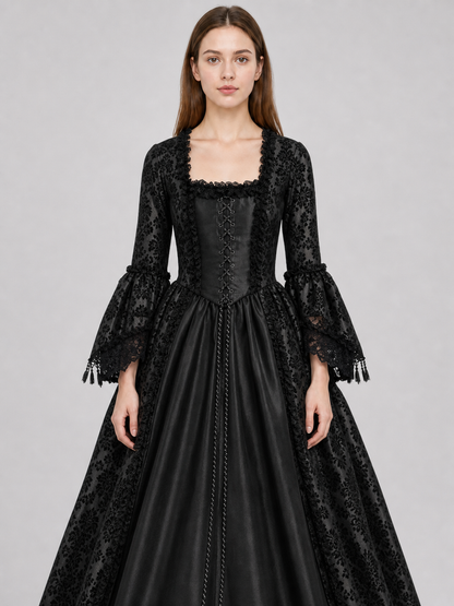 The black dress is designed in the aesthetic of a Victorian-era Gothic costume. The model features a floor-length silhouette, a fitted bodice with a square neckline, and decorative lacing or trim on the front. The long flared sleeves end in