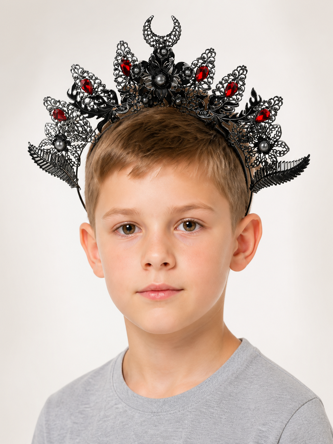 Close front view of a black and silver-look horned headpiece with red stones, filigree decorations, and pearl-like beads on a child