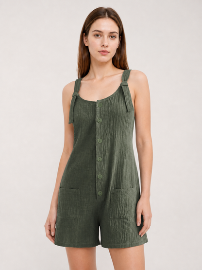 Upper-body close-up of olive green textured overall shorts, showing tied shoulder straps, a rounded neckline, front buttons and two pockets